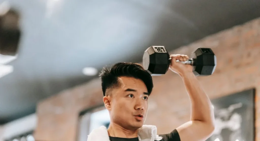 Jeune sportif ajuste des haltères de 20kg assis sur un banc d’entraînement
