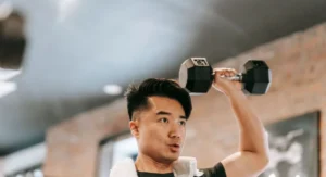 Jeune sportif ajuste des haltères de 20kg assis sur un banc d’entraînement