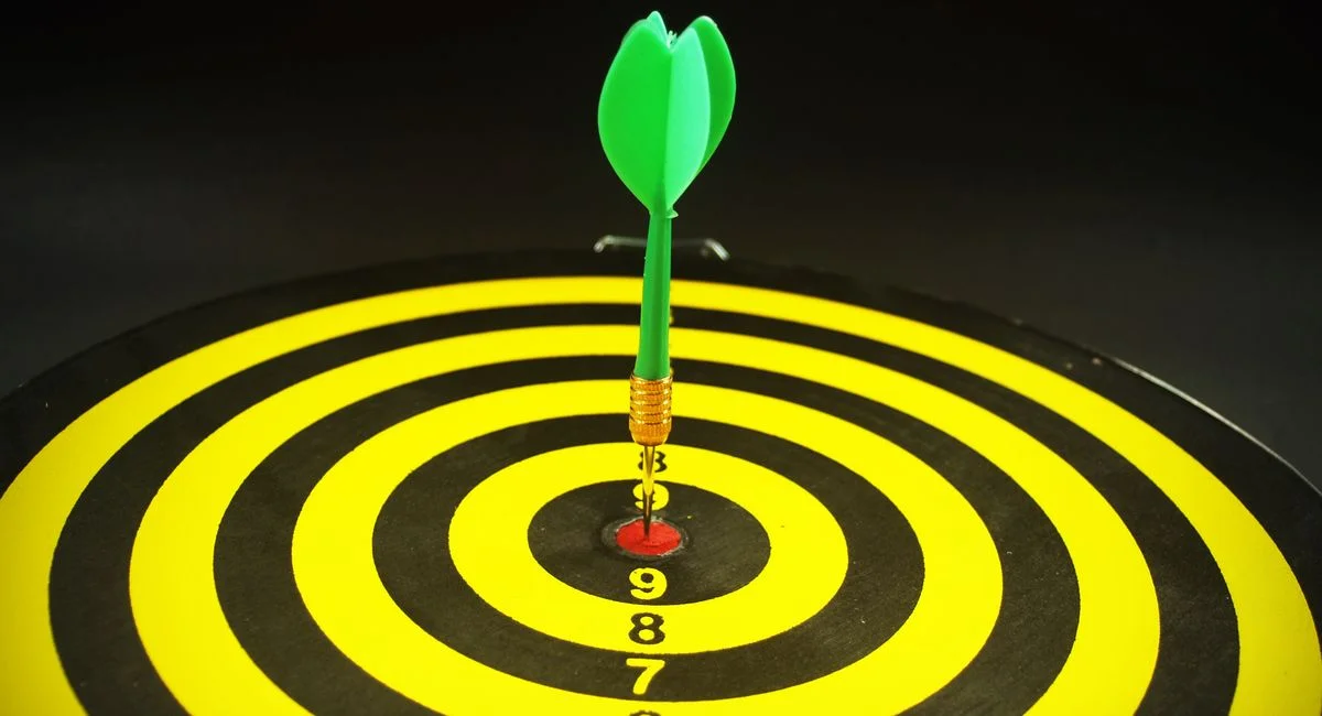 Close-up of a green dart hitting the bullseye on a yellow and black target board, symbolizing precision and success.