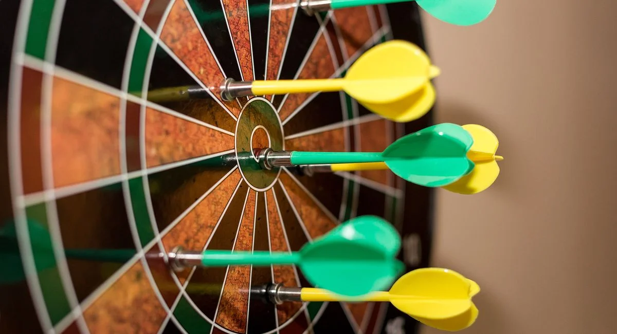 Multiple green and yellow darts precisely hitting a dartboard bullseye, indoor sport scene.